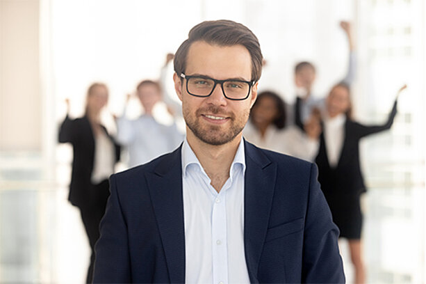 Junger Mann im Anzug vor einem jubelnden Business-Team