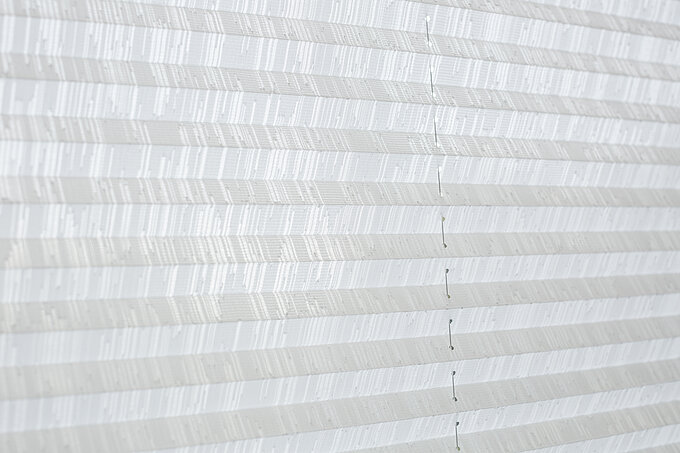 Detailaufnahme eines weissen Plisseestoffs mit feinem Streifenmuster und sichtbarer SchnurfĂźhrung.