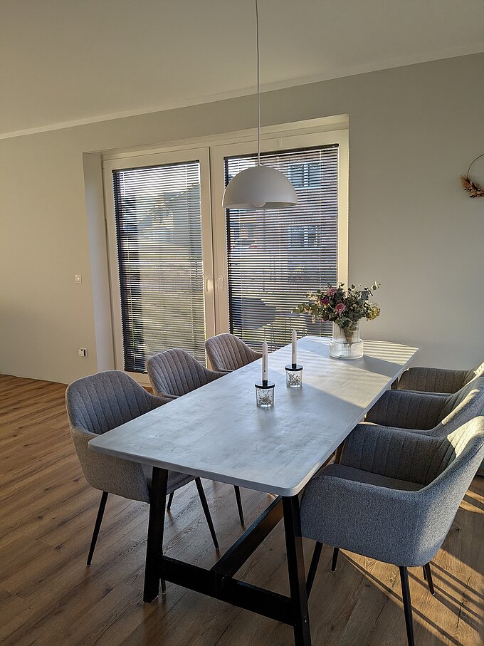 Esszimmer mit hellem Tisch und bodentiefen Fenstern, an denen geöffnete Twinline-Jalousien montiert sind.