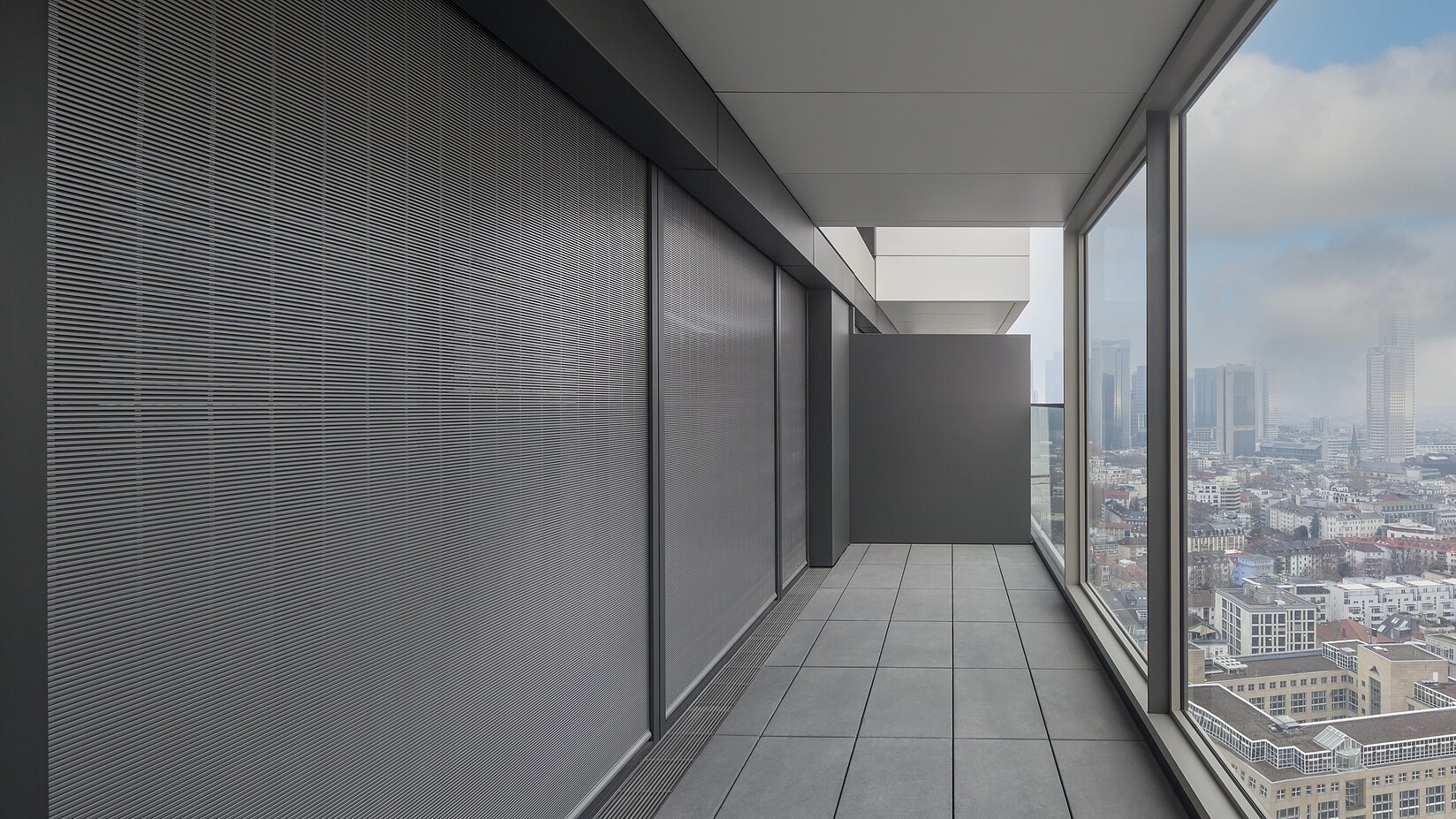 Balkon mit geschlossenem MHZ Metallbehang S_enro links und Ausblick auf die Stadt durch Glasfassade rechts.