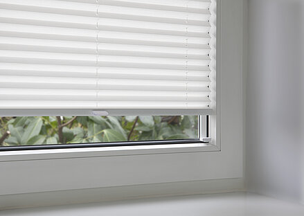 Weisses Plissee mit Klebeset in der Glasleiste eines Fensters montiert, Detailaufnahme.