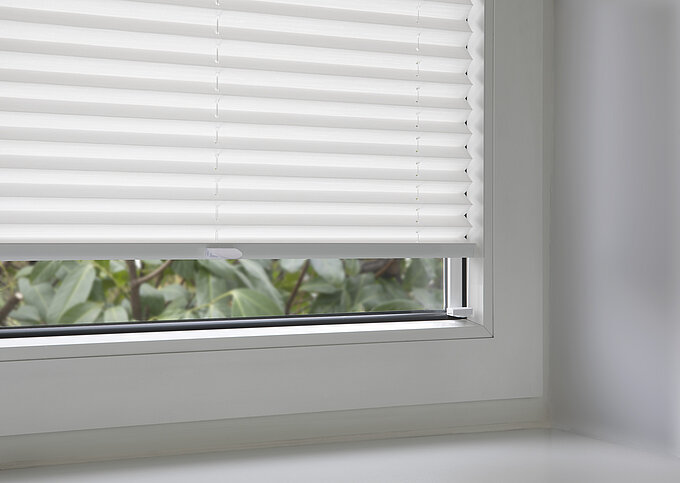 Weisses Plissee mit Klebeset in der Glasleiste eines Fensters montiert, Detailaufnahme.