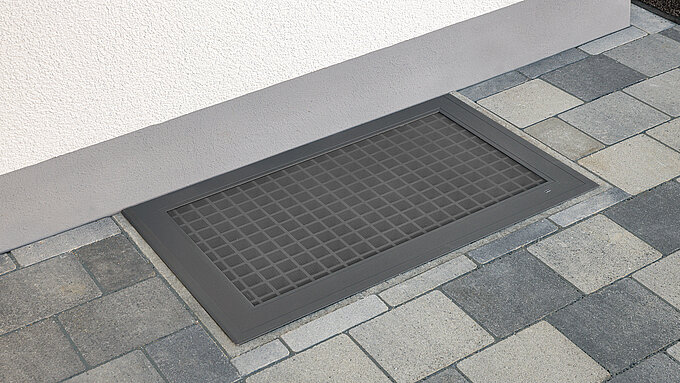 Lichtschachtabdeckung mit integriertem Edelstahlgitter vor einer Hauswand installiert.