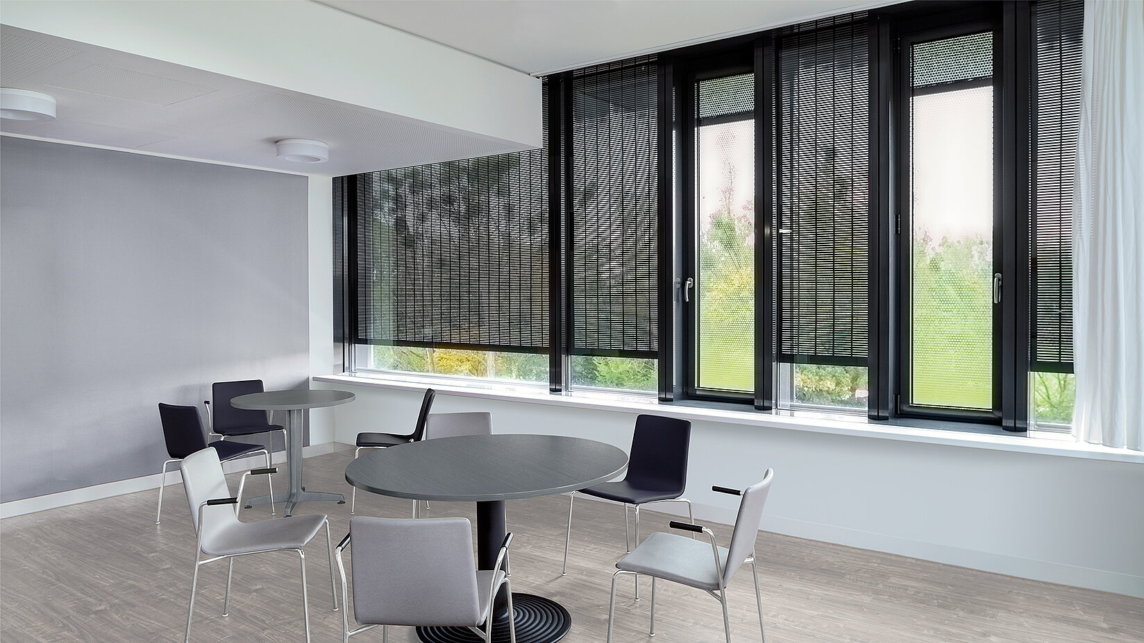 Aufenthaltsraum mit grossen Fenstern und Metallbehang Sonro als blendfreier Sicht- und Sonnenschutz.