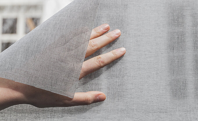 Hand zieht strukturiertes SQUID® Hafttextil leicht von der Glasscheibe ab.