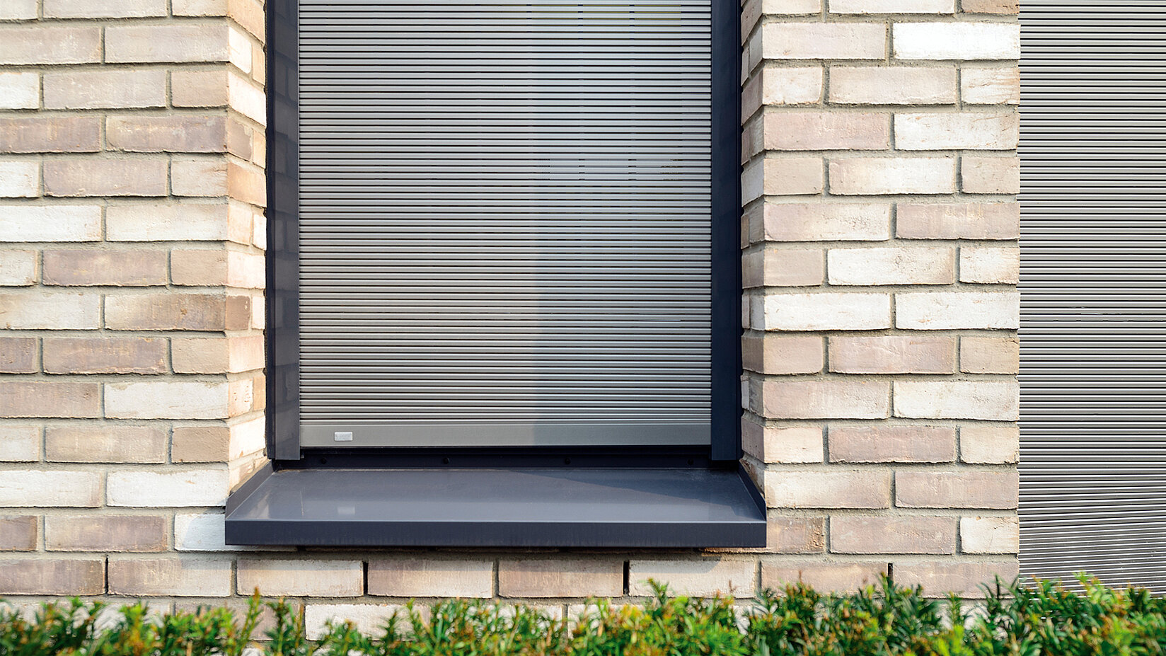 Aussenansicht eines Fensters mit geschlossenem Metallbehang Sonro in heller Ziegelfassade.