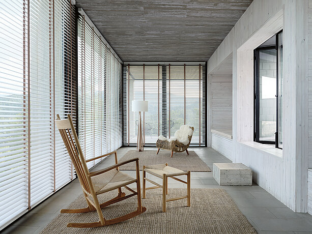 Heller Raum mit Holzjalousien, Schaukelstuhl und natürlicher Einrichtung im skandinavischen Stil.